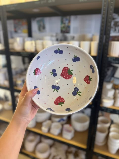 Handbemalte Schale mit Erdbeeren und Blaubeeren vor dem Keramikregal